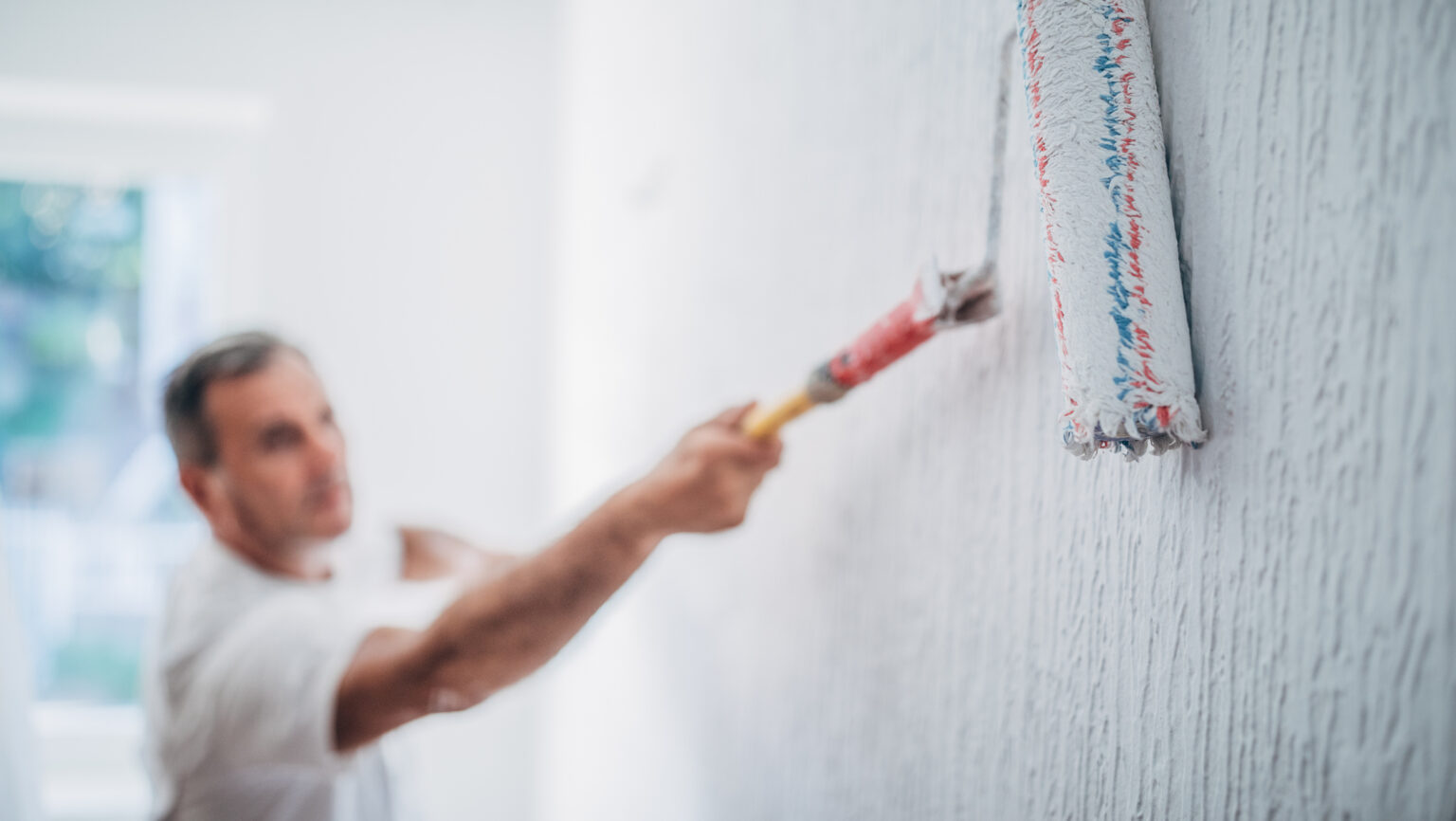 Maler i arbeid med en malerulle. Foto.