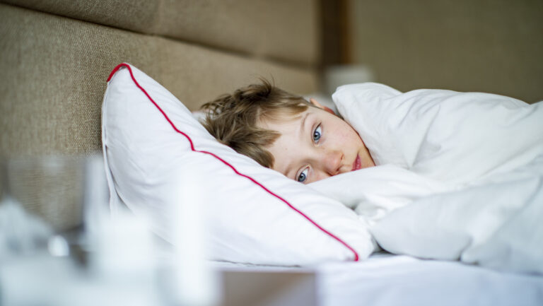 Barn ligger i sengen på grunn av sykdom, noe som kan føre til fravær fra skolen. Foto.