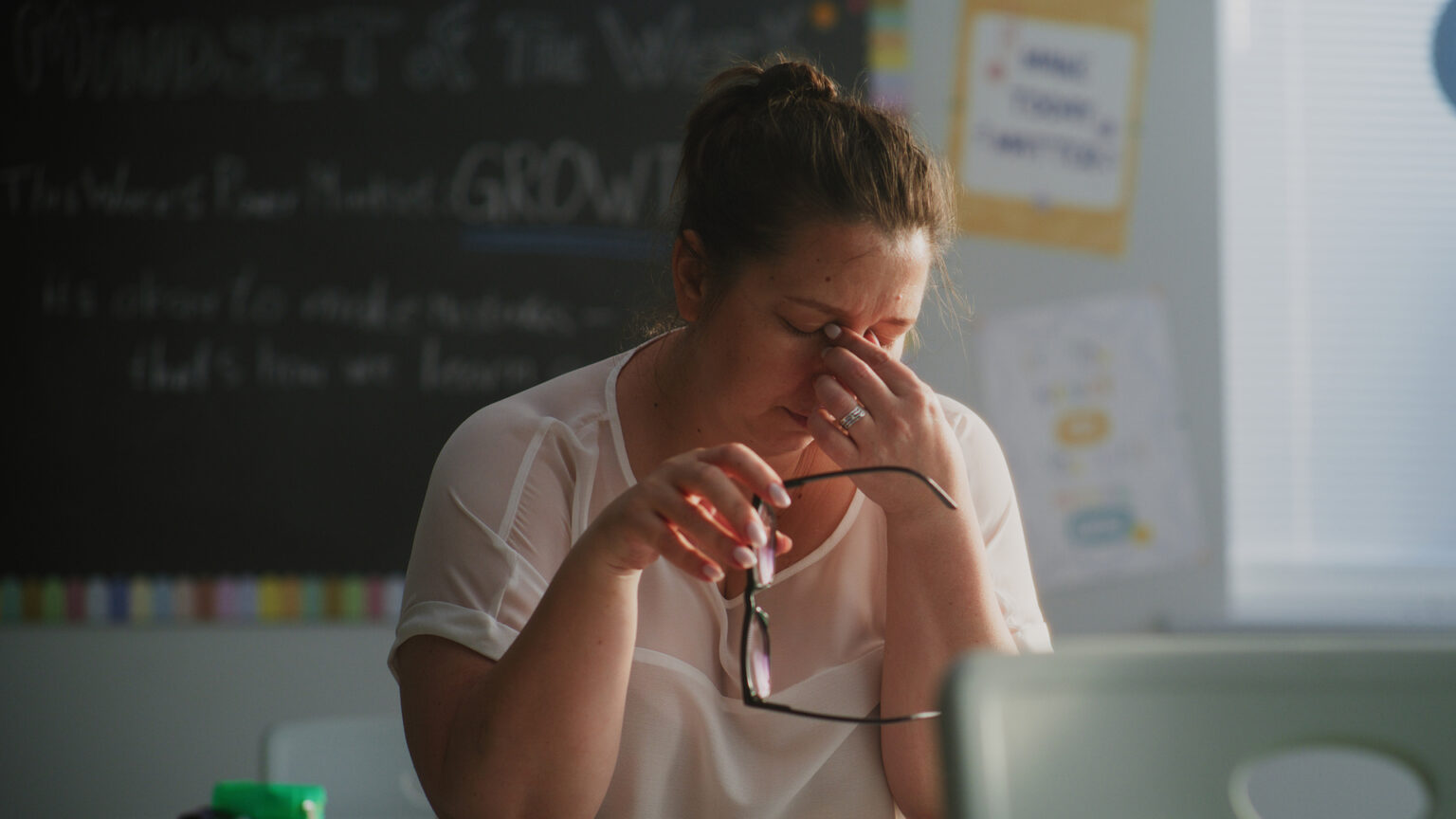 Sliten kvinnelig lærer sitter alene ved kateteret i et tomt klasserom og slapper av etter timen. Kvinnen opplever stress, utbrenthet og mental utmattelse i skolemiljøet, og jobber i barneskolen. Foto.